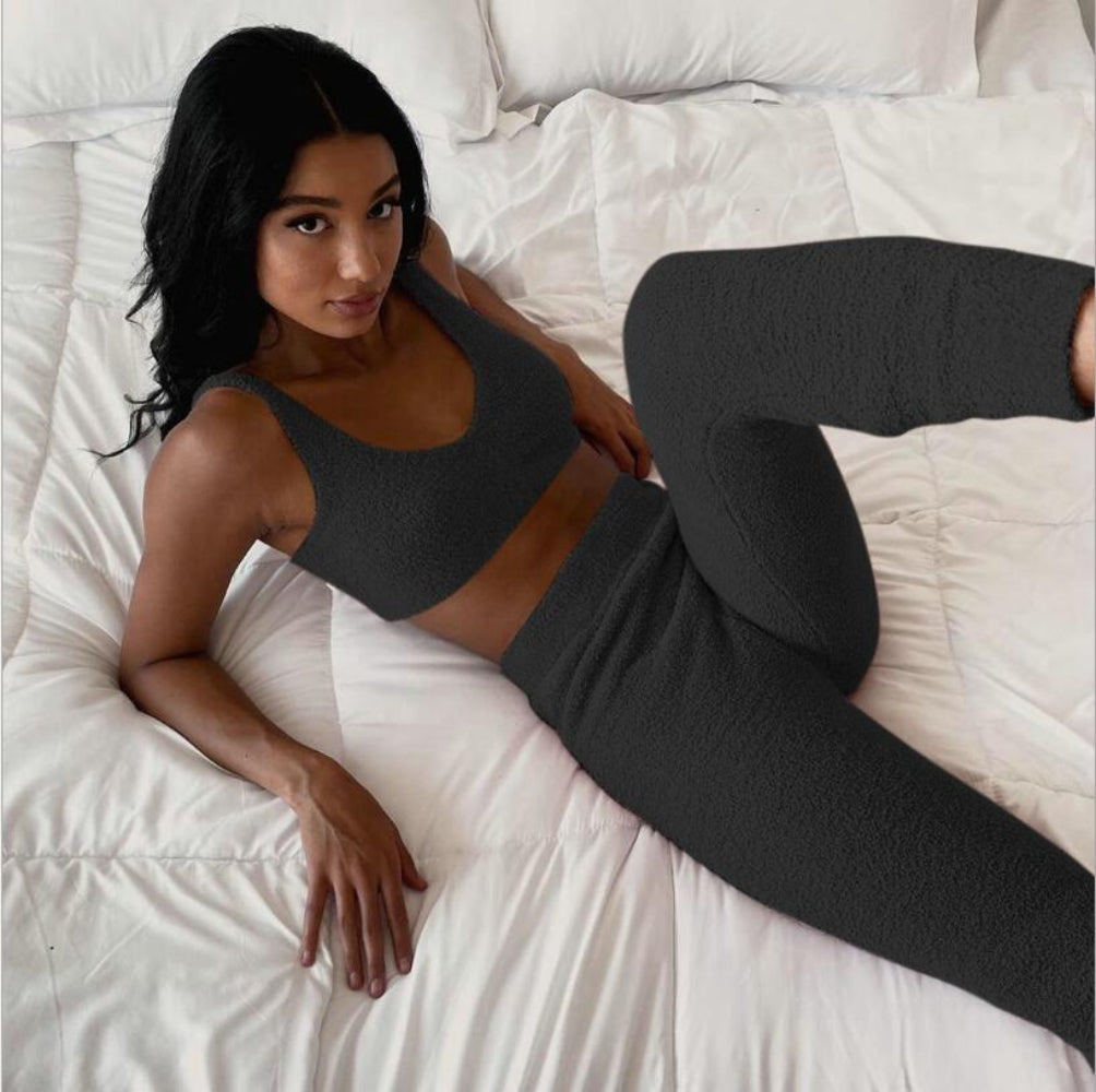 Woman wearing a dark gray sports bra and leggings lying on a white bed.