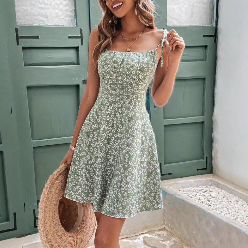 Woman wearing a green floral dress holding a straw bag in front of a green door.